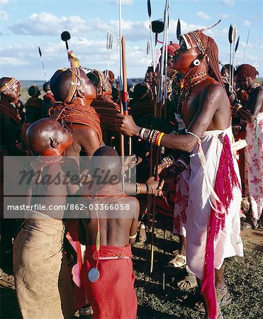 During Samburu wedding celebrations,warriors resplendent with long Ochred braids dance with young girls who have put on all their finery for the occasion. Both warriors and girls smear their faces,necks and shoulders with red ochre mixed with animal fat to enhance their appearance. Two spears are tipped with ostrich-feather pompoms.