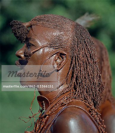 A Maasai warrior has daubed himself with red ochre mixed with animal fat to participate in a dance. His long ochred braids have been drawn forward from the crown of the head and tied in three places. This singular hairstyle sets warriors apart from the rest of their society.
