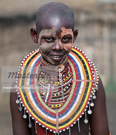 A young Maasai girl wears face paint and numerous beaded ornaments in preparation for a dance with warriors.