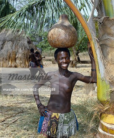 A Giriama girl from Kenya's Coast Province carrying a gourd full of water on her head. Her small skirt is made from strips of printed cotton material.