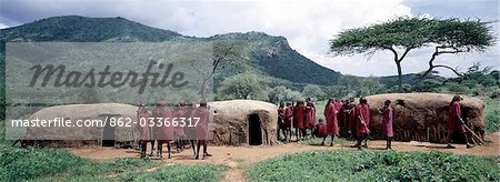 A group of Maasai warriors,resplendent with long Ochred braids,chat outside their traditional houses. These squat houses with rounded corners have roofs plastered with a mixture of soil and cow dung,so need regular repairs during rain.