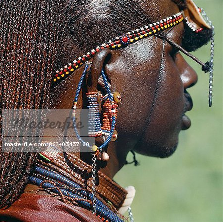 Detail of a Maasai warrior's ear ornaments and other beaded or metal adornments. The Maasai practice of piercing ears in adolescence and gradually elongating the lobes is gradually dying out. This warrior's body and his long braids have been smeared with red ochre mixed with animal fat.