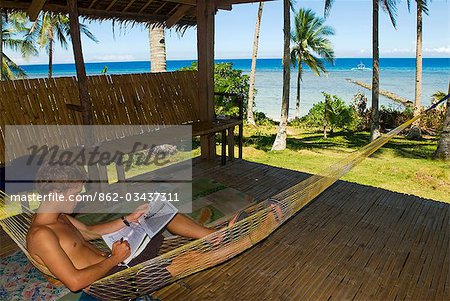 Philippines,Southern Leyte. Coral Cay Conservation volunteer relaxing in a hammock and studying dive plan charts. .