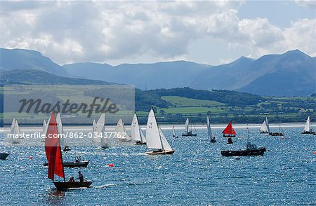 Wales,Anglesey,Beaumaris. Dinghies race during a regatta on the Menai Straits against the backdrop of the Snowdonia Mountains.