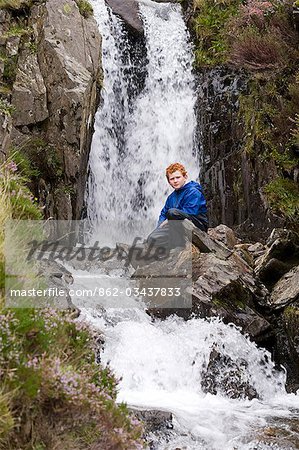 Wales,Conwy,Snowdonia. A young boy sits beside a waterfall in Cwm Idwal at the foot of the Glyders