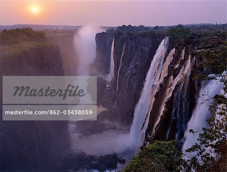 Sunset over the magnificent Victoria Falls. The Falls are more than a mile wide and are one of the world's greatest natural wonders. The mighty Zambezi River drops over 300 feet in a thunderous roar with clouds of spray.