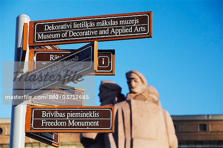 Tourist signpost with Statue of Latvian Red Riflemen in Town Hall square (Ratslaukums), Riga, Latvia