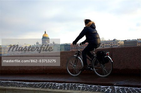 Russia, St.Petersburg; A cyclist passing in front of the Neva river with St.Isaac's Cathedral in the background
