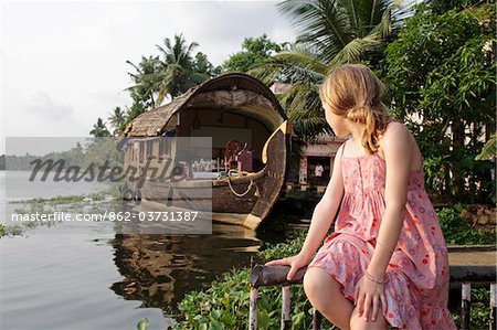 India, Kerala. Young girl on a family holiday in the Kerala Backwaters, a houseboat in the background.