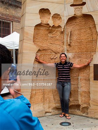 Australia, New South Wales, Sydney.  A tourist poses for a photo with a heritage sculpture at The Rocks district.