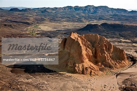 A crumbling extinct volcano, known as Aruba Rock, is surrounded by outflows of black lava rock on the edge of the Suguta Valley.