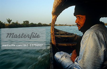 Mali. near Segou, Kalabougou. A Tuareg guide sits in a small boat, or pirogue, crossing the River Niger at Kalabougou. Mali. near Segou, Kalabougou. A Tuareg guide sits in a small boat, or pirogue, crossing the River Niger at Kalabougou.