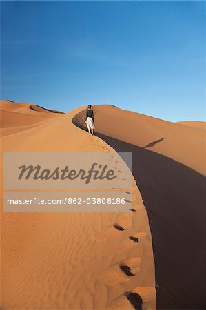 Oman, Empty Quarter. A young lady makes her way up the steep dunes. Oman, Empty Quarter. A young lady makes her way up the steep dunes.