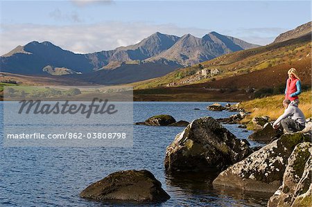 UK, North Wales, Snowdonia.  Man and woman stand on rocks at the edge of Llyn Mymbyr with the backdrop of The Snowdon Horseshoe.