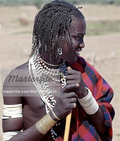 A Datoga young man in traditional attire.His braids are embellished with beads and aluminium can openers.Many of his white plastic bracelets are beautifully decorated with abstract and geometrical designs; long ago these bracelets would have been made of ivory.