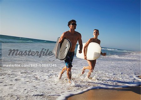 Young couple running out of ocean with bodyboards, Brighton beach, Perth, Western Australia, Australia