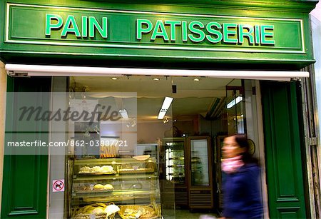 Arles; Bouches du Rhone, France; Young woman walking in front of a brightly coloured facade of a pain patisserie, a shop selling bread and confectionery.