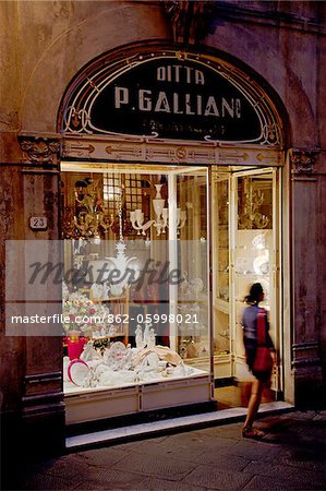 Italy, Tuscany, Lucca. Young woman walking in front of a shop in the historical centre.