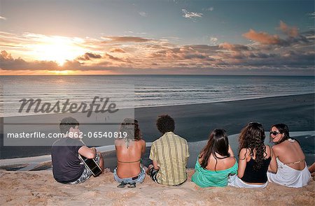 South America, Brazil, Ceara, Jericoacoara, a guitarist and a group of girls watch the sunset from the Sunset dune
