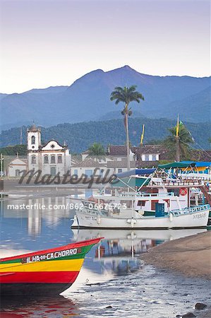Brazil, Parati, the Portuguese colonial town centre and the church of Saint Rita of Cascia seen from the water with colourful fishing boats moored on the quay