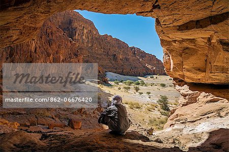 Chad, Elikeo, Ennedi, Sahara. A Toubou man looks out of a massive sandstone cave.