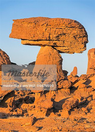 Chad, Chigeou, Ennedi, Sahara. A ridge of weathered red sandstone with a visitor giving scale to a giant mushroom-shaped feature.