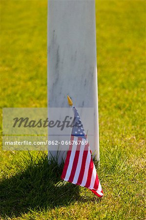 Memorial grave marker cross and Ameircan Stars and Stripes flag at the Normandy American Cemetery and Memorial, Omaha Beach, Colleville sur Mer, Basse Normandie, France.