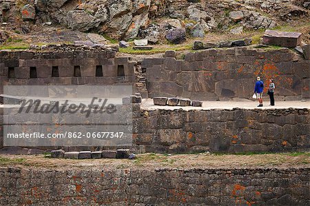 South America, Peru, Cusco, Sacred Valley, Ollantaytambo. Tourists in front of terraces of intricate stonework punctuated with trapezoidal alcoves at the Inca ruins