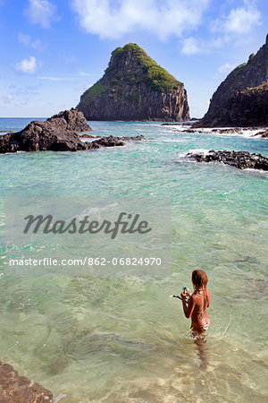 South America, Brazil, Pernambuco, Fernando de Noronha Island, a young woman snorkelling at the Bay of Pigs with the Two Brothers rocks behind MR