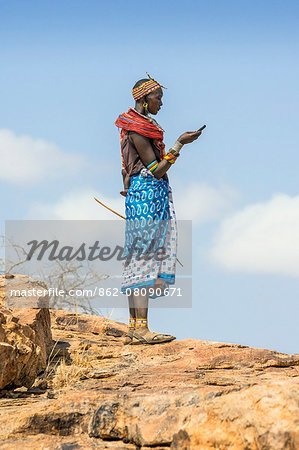 Kenya, Samburu County, Serolevi. A Samburu woman stands on a hill to make a phone call from her mobile phone. Kenya' s mobile phone network has revolutionised communications among rural communities.