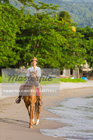Dominica, Portsmouth. A young woman rides a horse on Purple Turtle Beach. .