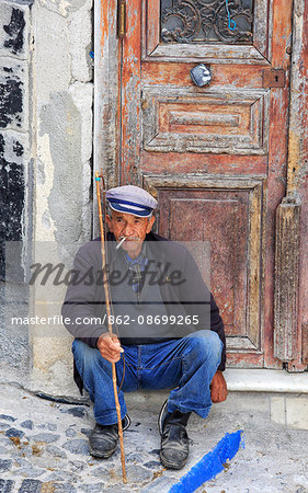 Greece, Santorini, Fira. Local man sitting and having a rest by a doorway in Fira town.