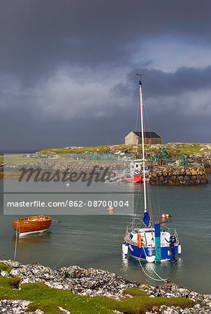 Scotland, Argyll and Bute, Isle of Tiree. Boats moored at Scarinish Harbour under a stormy sky.