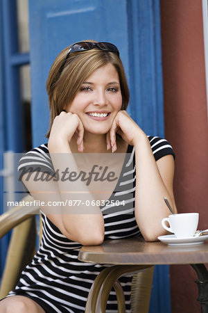 Young woman sitting at coffee shop terrace, posing for the camera, smiling