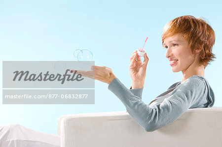 Portrait of woman on light blue background, playing with bubbles