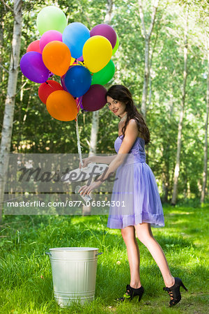 Young woman throwing away can, bunch of balloons tied to dustbin lid