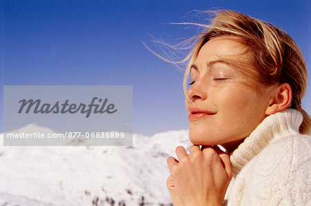 Smiling woman, eyes closed, joined hands, mountain at the back, portrait