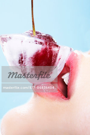 Young woman with a cherry in an ice-cube on her mouth