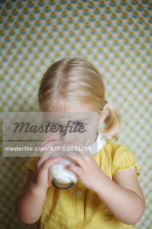 A 2 years old girl posing as she 's drinking a glass of milk