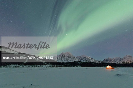 A tent in the snow lighted up by Northern Lights and starry sky in the polar night Svensby Lyngen Alps Tromsø Norway Europe