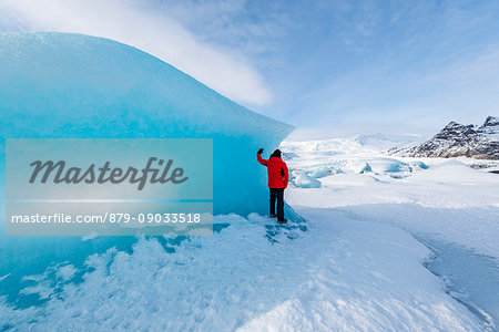 Fjallsarlon glacier lagoon, East Iceland, Iceland. Man with red coat admiring the view of the frozen lagoon in winter (MR).