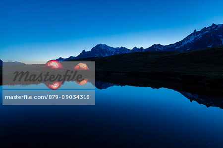 Camping tents reflected in the alpine lake at night Mont De La Saxe Courmayeur Aosta Valley Italy Europe