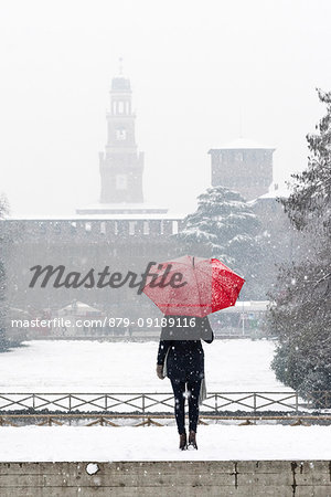 A woman with red umbrella admires the view of Sempione park during a snowfall. Milan, Lombardy, Italy, Europe.