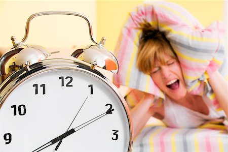 simsearch:6109-06194890,k - Close up of alarm clock. Young woman in the background covering ears with pillow. Stockbilder - Microstock & Abonnement, Bildnummer: 400-04020608