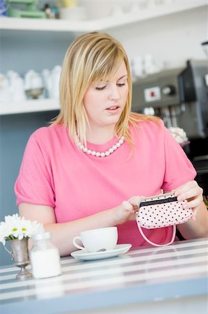 A young woman sitting in a cafe looking worried into her purse Stock Photo - Budget Royalty-Free & Subscription, Code: 400-04037726