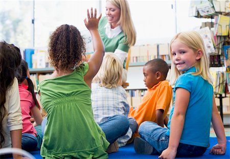 students with hands raised in classroom with female teacher - Kindergarten teacher reading to children in library, girl lookin Stock Photo - Budget Royalty-Free & Subscription, Code: 400-04037807