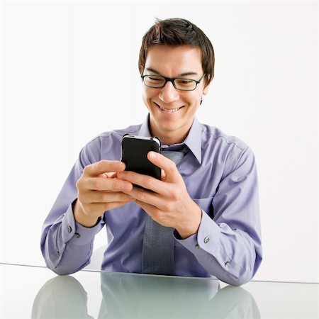 simsearch:400-04186486,k - Smiling Asian businessman sitting at desk texting using his pda cellphone. Stock Photo - Budget Royalty-Free & Subscription, Code: 400-04039914