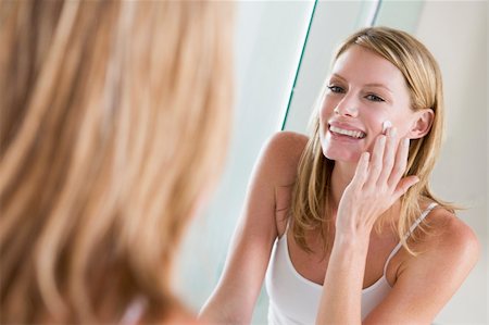 Woman in bathroom applying face cream smiling Stock Photo - Budget Royalty-Free & Subscription, Code: 400-04043329