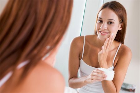 Woman in bathroom applying face cream smiling Stock Photo - Budget Royalty-Free & Subscription, Code: 400-04043336