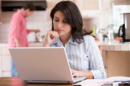 Woman in kitchen with paperwork using laptop with man in backgro Stock Photo - Budget Royalty-Free & Subscription, Code: 400-04043660